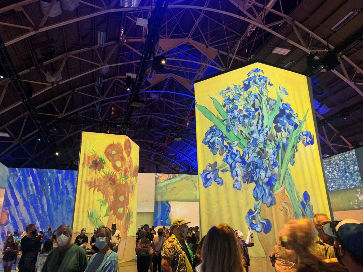 Sunflowers and irises , set against a tapestry of various Van Gogh paintings along the walls of the room.